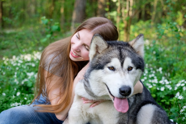 Redhead young woman plays with her dog malamute on a walk in the forest