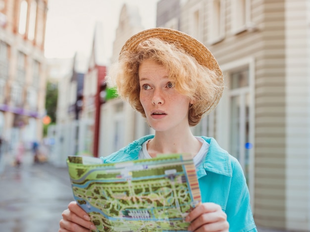 Фото Рыжая молодая женщина путешествует по западной европе и использует бумажную карту в неизвестном городе