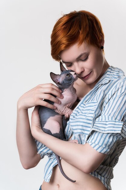 Redhead young woman with closed eyes gently hugs cat looking at owner Studio shot white background