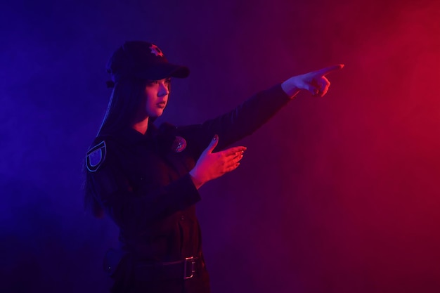 Redheaded female police officer is posing for the camera against a black background with red and blu...