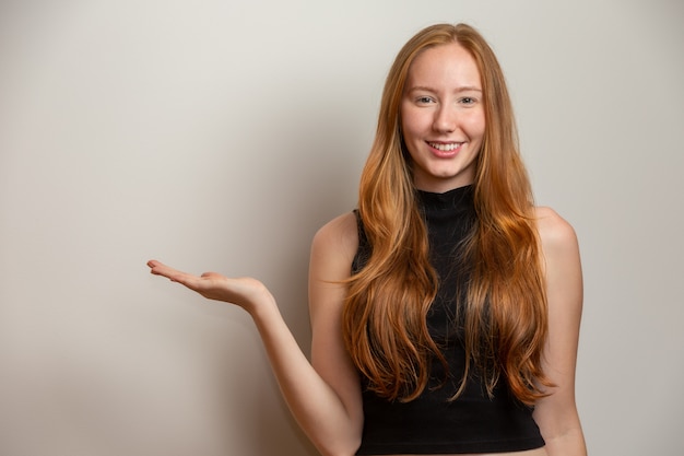 Una ragazza dai capelli rossi sul muro bianco offre opportunità puntare il dito sul lato dello spazio libero copia per l'annuncio di contenuti promozionali.