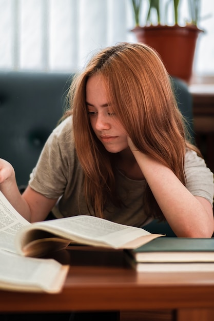 公共図書館で本を読んでいる興味のある表情を持つ赤毛の少女。