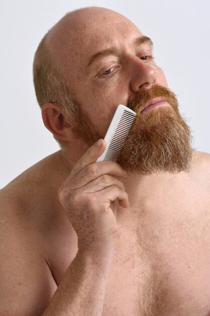 Redheaded man combing his beard on white background