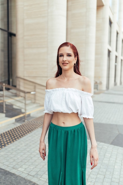 Redheaded woman in summer clothes in front of a building posing for the camera.