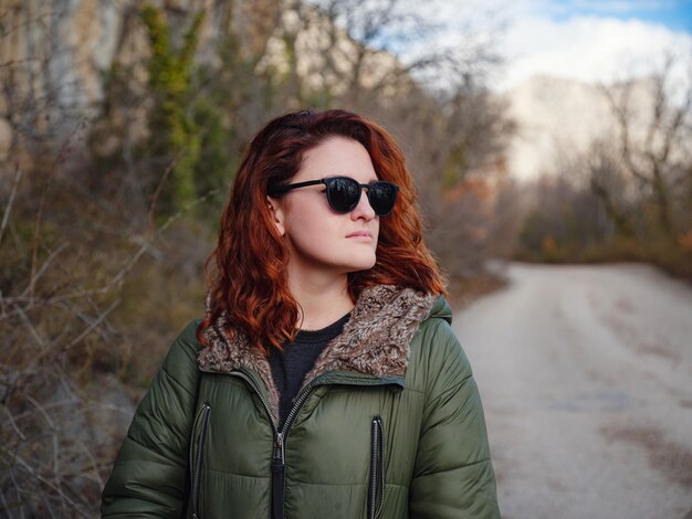 A redheaded woman walking along a mountain road in early spring