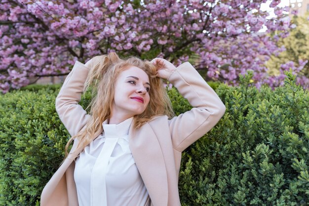 写真 桜の花の庭の赤い少女 美しい若い白人の女性が 公園で春の日を楽しんでいます