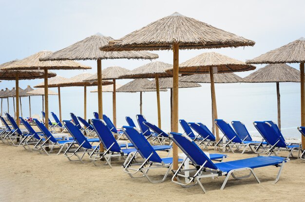 Reed-parasols en ligstoelen bij het strand