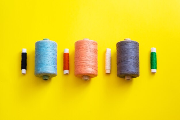 Reels with threads of different colors and sizes on a bright, colorful background. flat lay