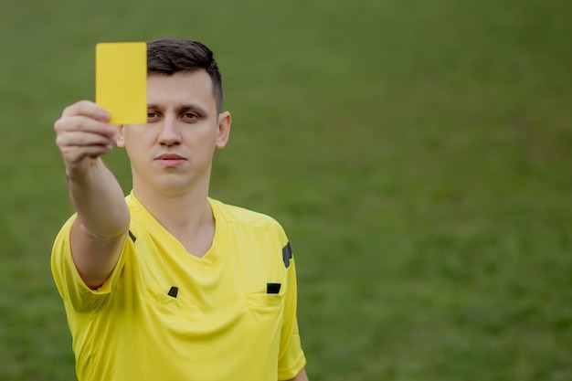 Photo referee showing a yellow card to a displeased football or soccer player while gaming. concept of sport, rules violation, controversial issues, obstacles overcoming.