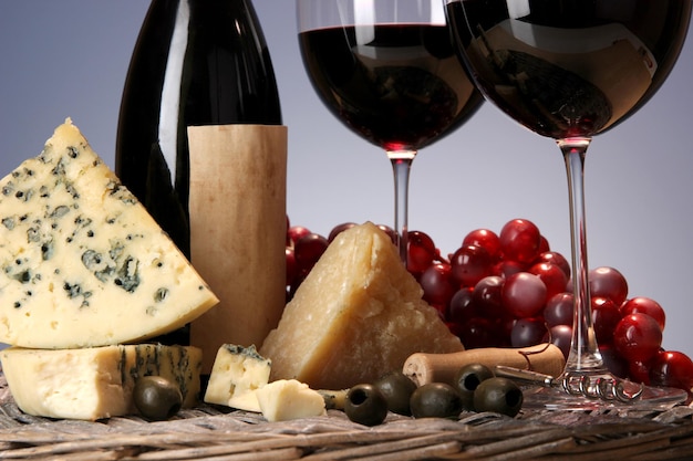 Refined still life of wine cheese and grapes on wicker tray on wooden table on blue background