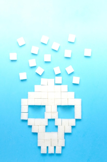 Refined sugar on blue backgroundSugar cubes in form of skullConcept of healthy eating addiction to candyCloseup