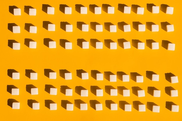 Refined sugar cubes lines on yellow background top view