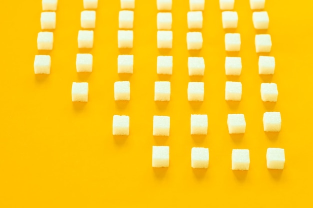 Refined sugar on yellow backgroundCubes of sweet and white sugar in geometricshape Hard shadows