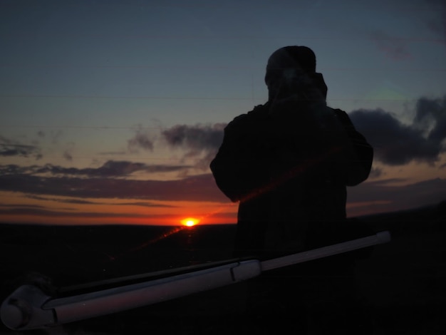 Reflectie in de achterruit van een kleurrijke zonsondergang en het silhouet van een fotograaf.