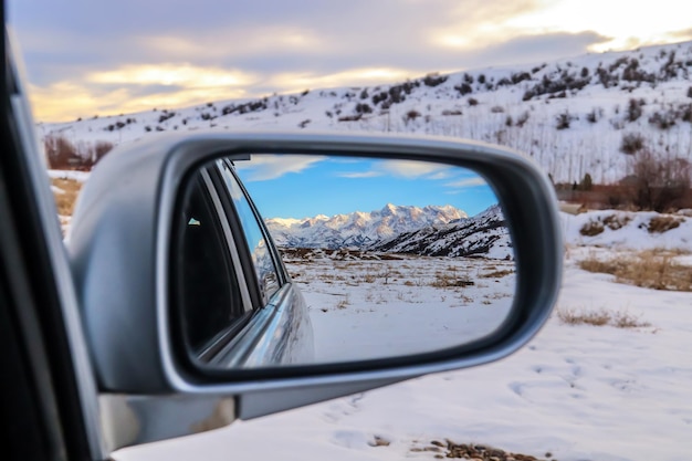 Reflectie in de spiegel van een auto van prachtige besneeuwde bergen en wegen