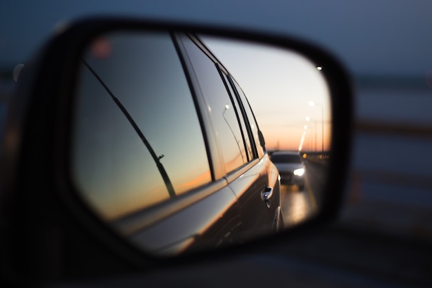 Reflectie in de spiegel van een auto weg met vervoer bij zonsondergang