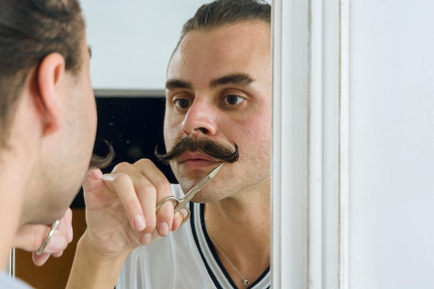Reflectie in de spiegel van een niet-binaire Latijns-persoon die zijn snor met een schaar repareert