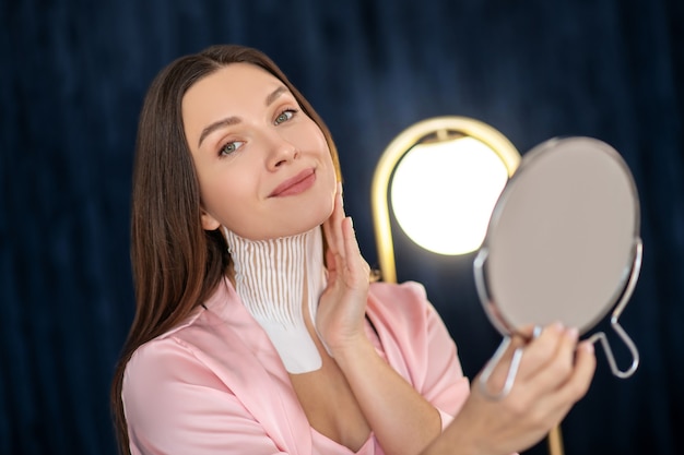 Reflectie. Jonge vrouw in roze lingerie en met banden op haar nek in de spiegel kijken en glimlachen