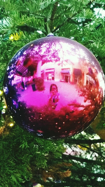 Foto reflectie op vrouw op roze ornament hangend op kerstboom