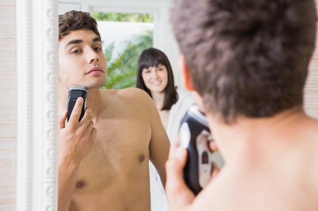 Reflectie van de jonge man in spiegel scheren met elektrisch scheerapparaat