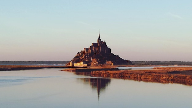 Reflectie van de Mont Saint-Michel in de rivier tegen een heldere hemel bij zonsondergang
