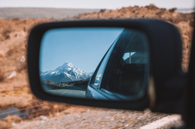 Reflectie van een met sneeuw bedekte berg in de zijkantspiegel van een auto