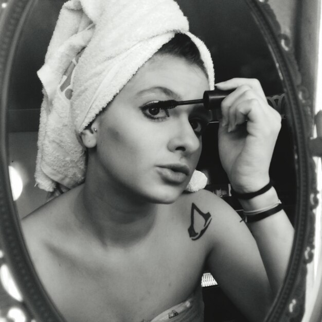 Foto reflectie van een vrouw in de spiegel die mascara aanbrengt