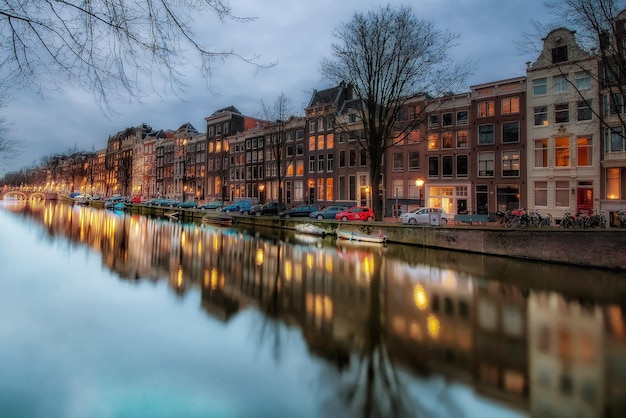 Reflectie van verlichte gebouwen en kale bomen in het kanaal bij zonsondergang
