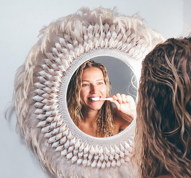 Photo reflection of beautiful woman brushing teeth seen through mirror