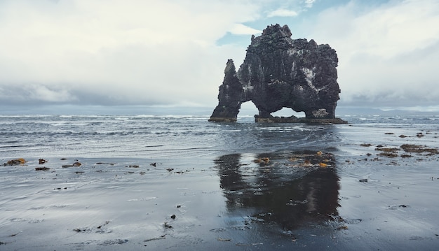 Reflection in the black sand of the sky and a large rock with arches on the coast. HvÃ­tserkur Rock