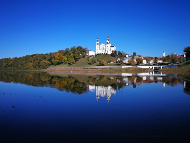 Reflection of buildings in lake against clear blue sky