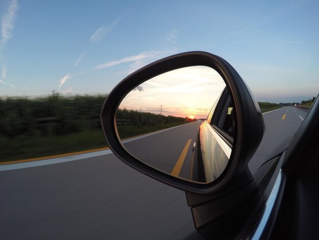 Foto riflessione dell'auto sullo specchio laterale durante il tramonto