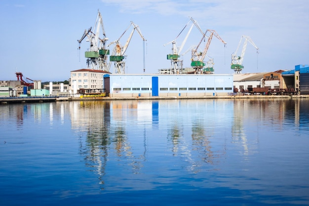 Reflection of cranes at commercial dock in sea against sky