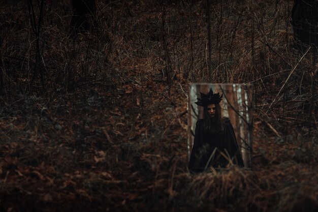 Riflessione di una strega spaventosa scura in uno specchio in una foresta cupa