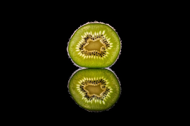 Reflection of fresh ripe kiwi fruit slice placed on black mirrored background in studio