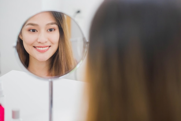 사진 아름다운 미소 아시아 여성 블로거의 거울에 비친 반사는 건강한 얼굴 개념을 위해 홈스킨케어에서 화장품을 만들고 사용하는 방법을 보여주고 있습니다