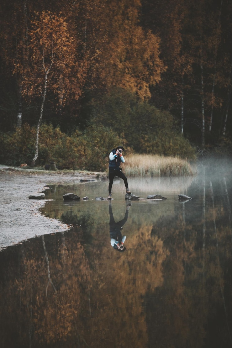 Photo reflection of man photographing on lake in forest