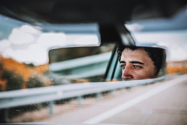 Photo reflection of man in rear-view mirror of car