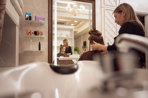 Foto riflessione sullo specchio della giovane donna che ottiene taglio di capelli dal parrucchiere adulto elegante nel salone di bellezza