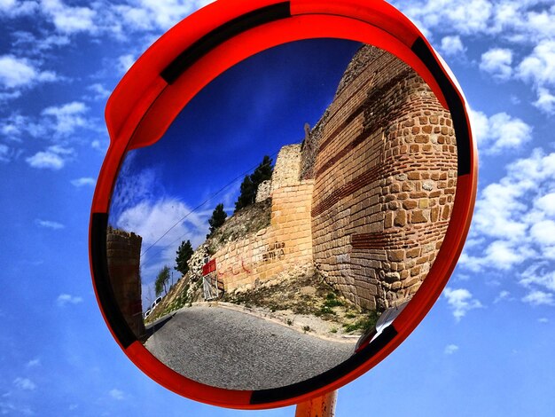 Reflection of old ruins on road mirror against blue sky