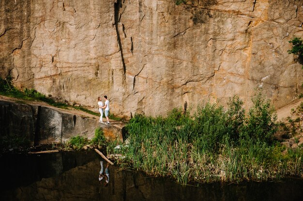 Reflection of people stand and hug near lake on background of rocks