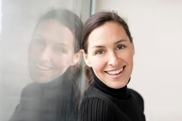 Reflection and portrait of smiling businesswoman wearing black turtleneck pullover