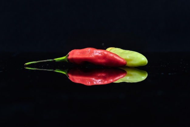 Foto riflessione di peperoncini rossi e gialli su uno sfondo nero