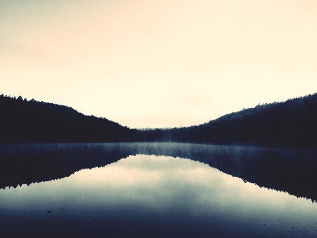 Photo reflection of silhouette hills on calm lake against sky at dusk