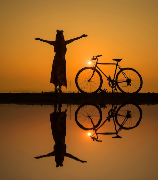Photo reflection of silhouette woman with bicycle in lake against sky during sunset