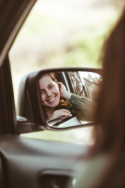 Reflection on stunning smiling woman in car rear mirror