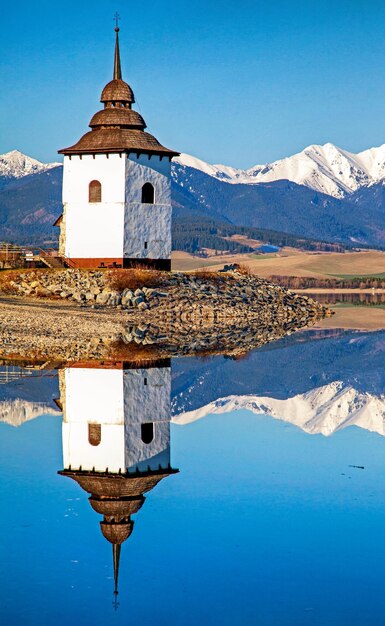 Reflection of tower of church on water surface of lake Snowy mountains at background