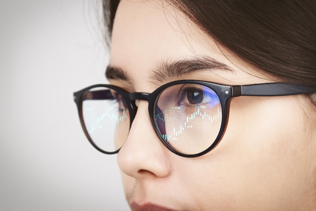 The reflection of the trader39s market charts in the glasses of a girl looking at a computer monitor