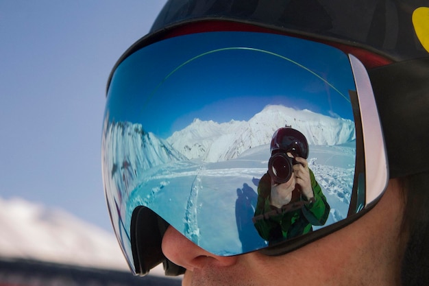 Reflection of a traveler photographer wearing a large ski mask in the winter mountains