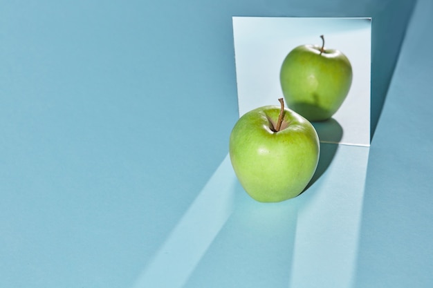 Reflection of a whole green apple in the mirror and shadow